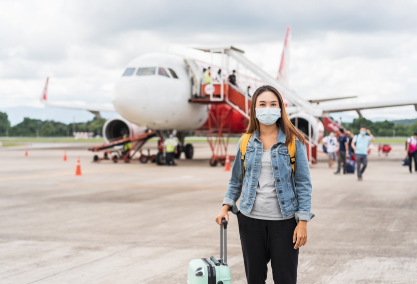 international traveling nurse with a mask, backpack, and suitcase boarding a plane to her next assignment