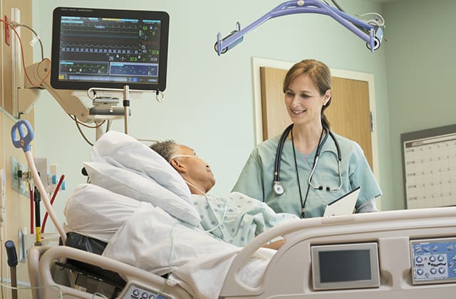 Page Image 1: A CVICU nurse smiling at and attentively monitoring a patient in a hospital bed, surrounded by medical equipment and monitors displaying vital signs